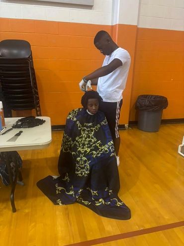 A young boy getting a haircut in a gymnasium with orange walls.