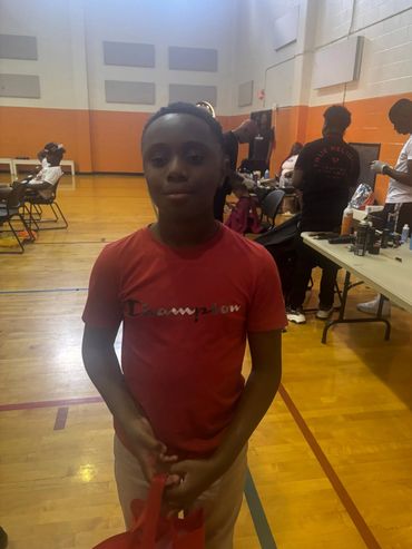 A boy in a red Champion shirt stands in a gym with people in the background.