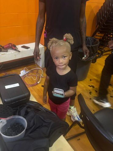 A young girl holding a phone stands in a room with wooden flooring and orange walls.