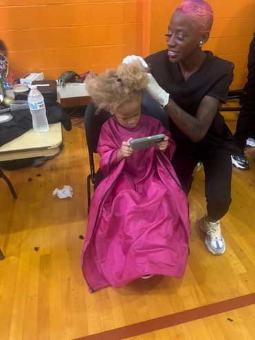 A child getting a haircut while playing on a phone, with a stylist smiling.