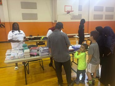 People distributing school supplies in a gymnasium.
