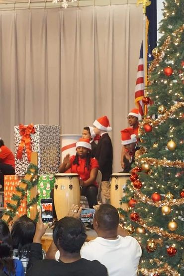 Children in Santa hats play drums during a festive Christmas performance.