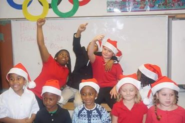 Children wearing Santa hats posing happily in a classroom holiday show setting.