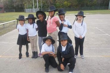 A group of children wearing black hats and mixed outfits pose outdoors on a concrete surface.