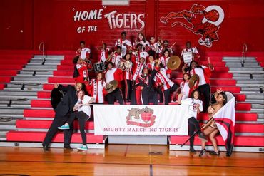 High school marching band posing proudly in red and white uniforms in a gymnasium.