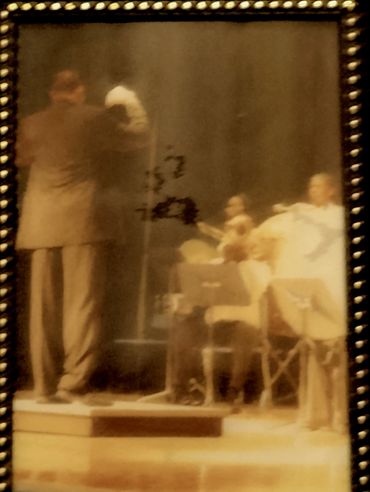Blurry vintage photo of a man and musicians on stage.