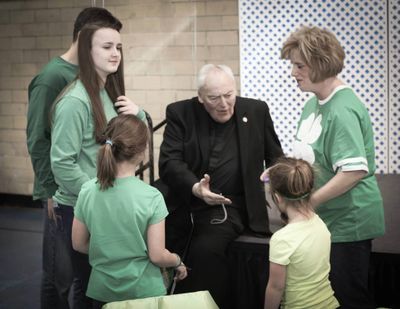 Rev, John P. Smyth holding his had out to children dressed for St. Patricks Day.