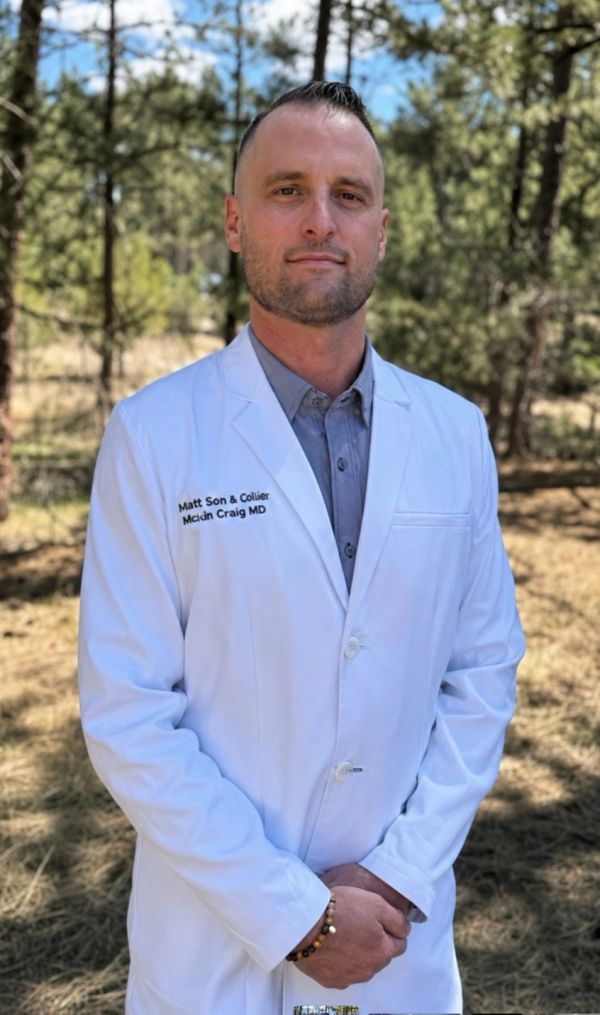 Man in a white lab coat standing outdoors.