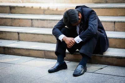 Businessman in suit sitting on stairs, head down, looking stressed.
