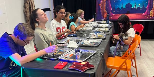Children engaged in a bead crafting activity at a long table.