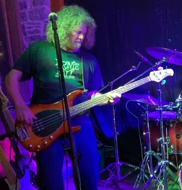 Musician playing bass guitar on stage under colorful lights.
