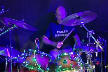 Drummer playing with intensity, wearing a 'FAILED MUSICIAN' shirt.