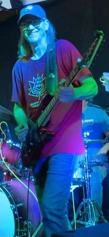 Man playing electric guitar on stage with drums in the background.