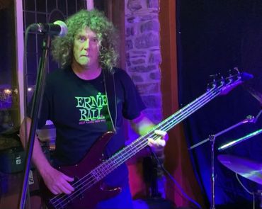 Musician playing bass guitar on stage with purple lighting.