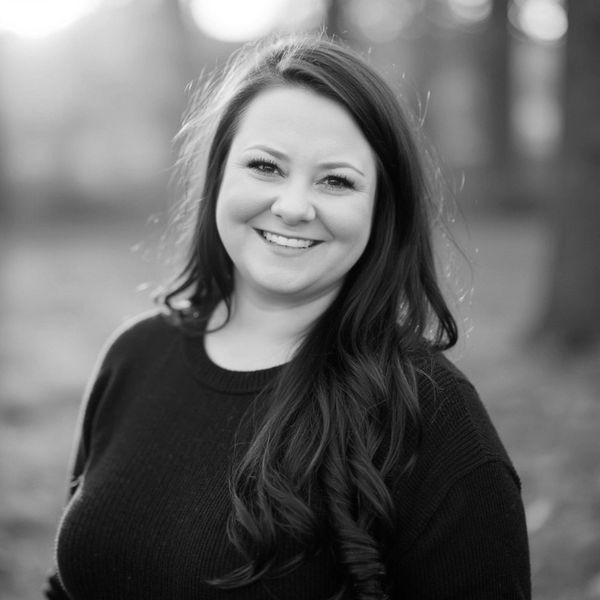 Smiling woman with long hair in a black sweater outdoors.