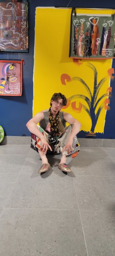 Young man sitting on the floor in front of colorful abstract paintings.