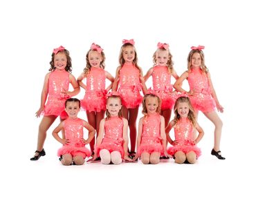 Young girls in sparkly pink dance costumes posing together on a white backdrop.