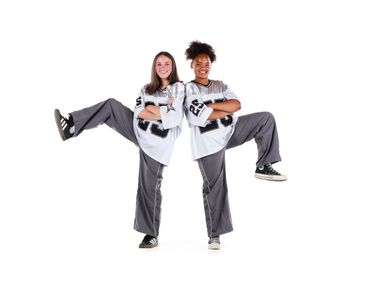 Two young dancers in matching outfits posing with one leg raised.