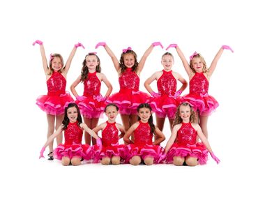 Young girls in red sparkle dance costumes posing cheerfully in a group.