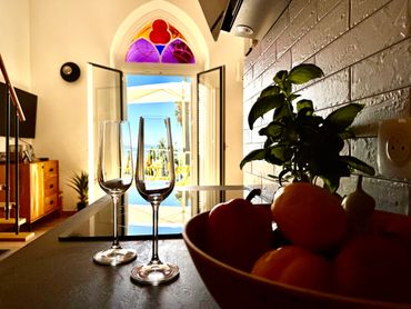 Two empty wine glasses on a table near a bowl of fruit with a bright doorway in the background.
