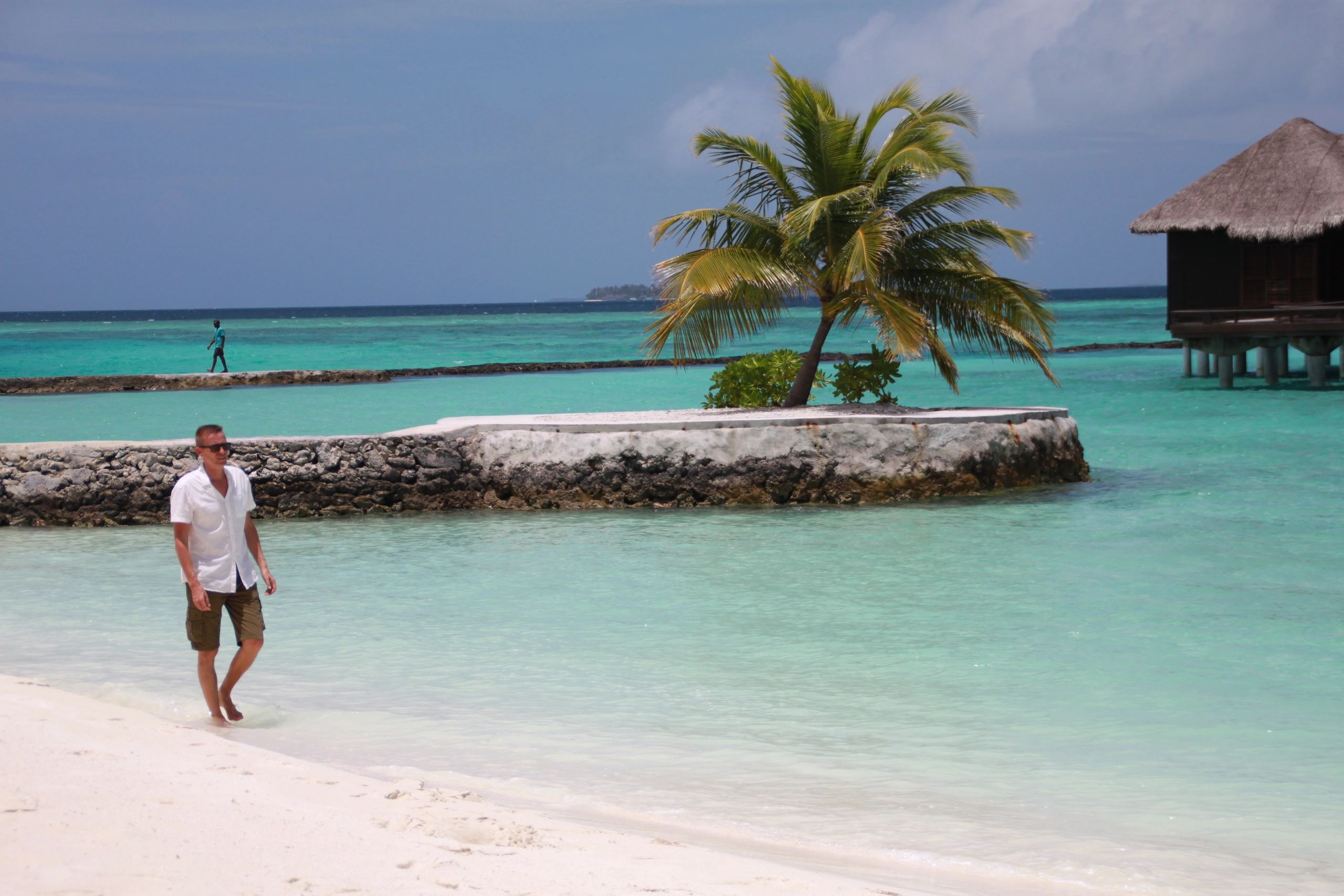 Author Jarmo Syväri walks on a white sandy beach in the Maldives: crystal waters and a palm tree.