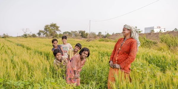 A smiling woman and six children in a lush green field.
