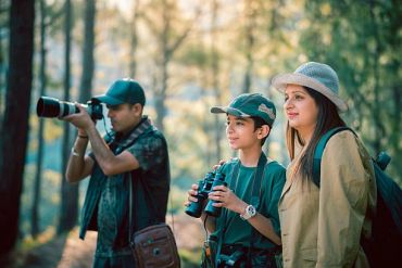 Family enjoying birdwatching in a forest with binoculars and camera.