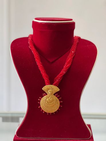 Traditional red beaded necklace with a gold pendant on a red velvet display bust.