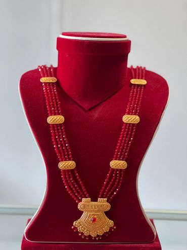 Traditional red bead necklace with gold pendant on red velvet display.