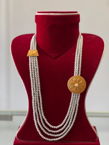 Elegant multi-strand pearl necklace with gold floral embellishments on a red velvet display.