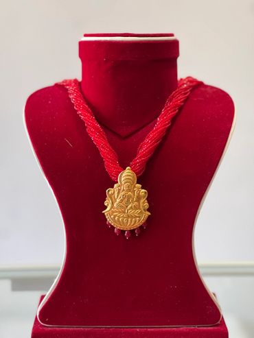 Gold pendant necklace with red beads on a red velvet stand.