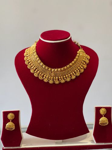 Intricate gold necklace and matching earrings set displayed on red velvet stands.