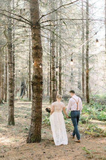 A couple walking through our forest wedding location. Looking out at the Edison lights. 