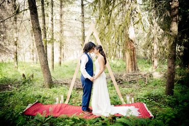 A couple getting married in the forest under an arch, on a Persian rug.