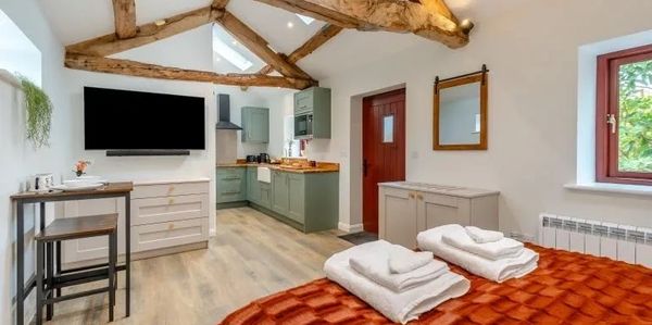 Cozy studio with exposed wooden beams, a small kitchen, and a warm bed.