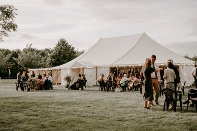 Outdoor gathering with a large white tent and people socializing.