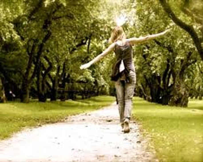 Young woman walking down a sunny footpath, with trees lining both sides