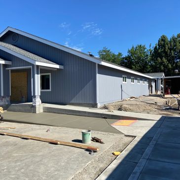 New concrete sidewalk being poured beside a blue house.