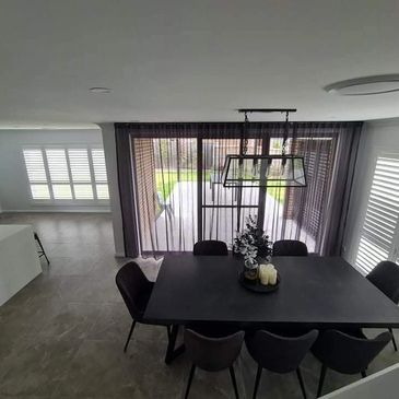 Modern dining area with black table and chairs, sheer curtains, and natural light.