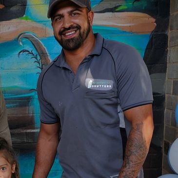 Smiling man in a gray shirt and cap stands in front of a colorful owl-themed backdrop.