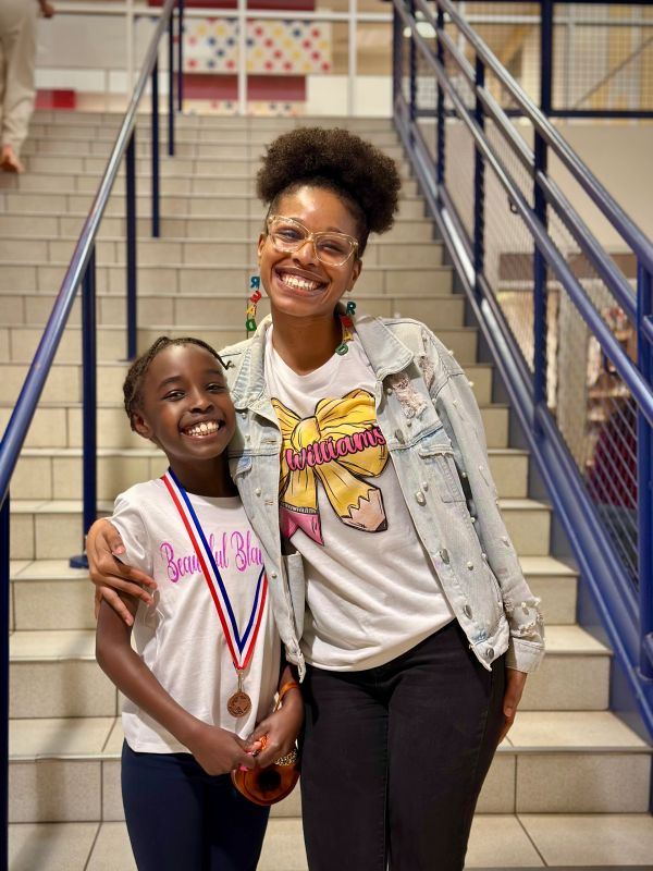Smiling girl with medal and woman posing on stairs.