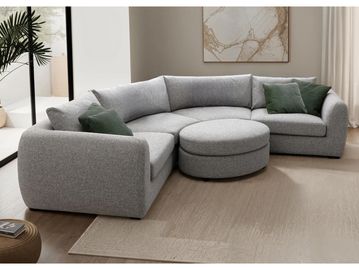 Modern gray sectional sofa with round ottoman and green accent pillows in a bright living room.