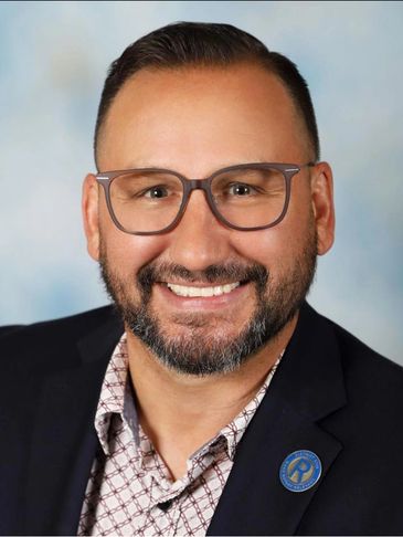 Smiling man with glasses in a blazer and patterned shirt.