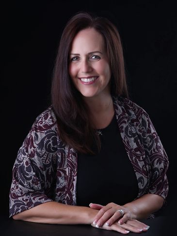 Smiling woman with long brown hair wearing a patterned shawl against a black background.