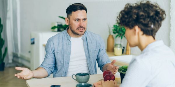 Two people having a serious conversation at a table with coffee cups.