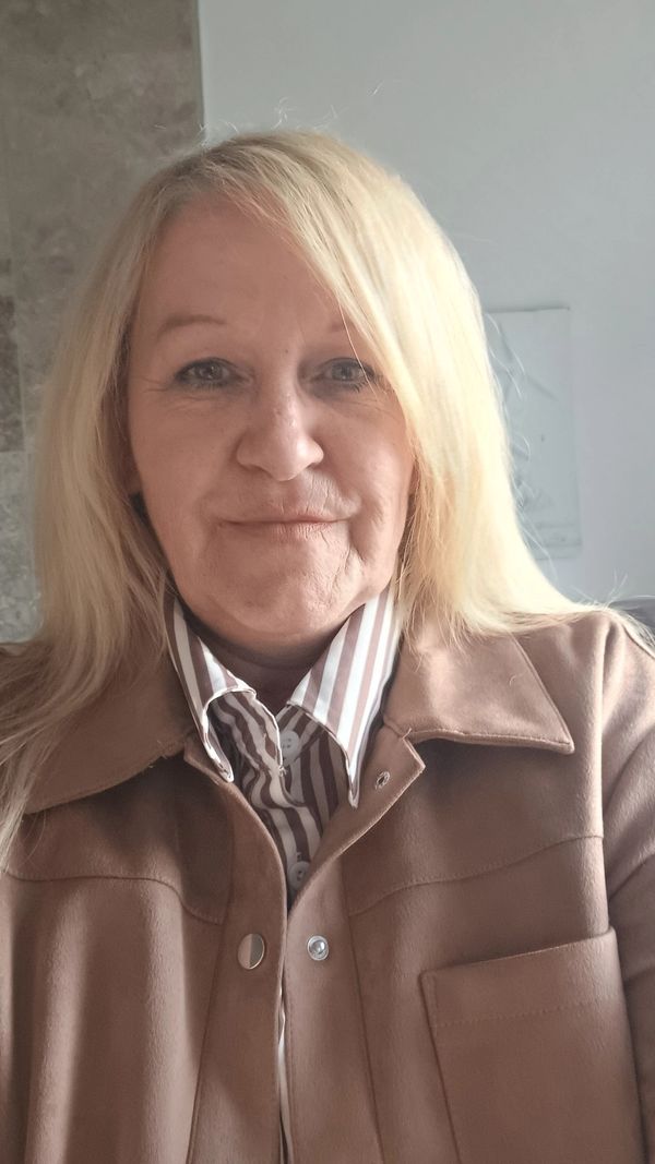 A woman with blonde hair wearing a brown jacket and striped shirt.