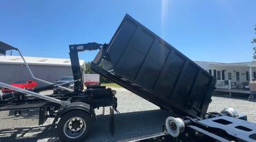 A black dump trailer is tilted for unloading under a clear blue sky.