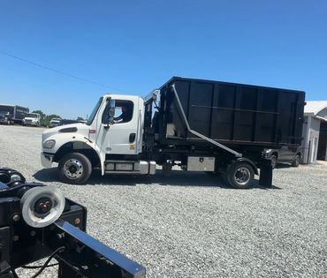 White truck with a large black container parked on gravel under clear blue sky.