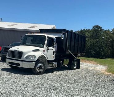 White dump truck with black container parked on gravel under clear blue sky.