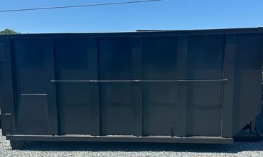 Large black dumpster on gravel under clear blue sky.